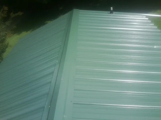 New green metal panels meeting at the ridge of a roof — Flat Roof Repair work by our crew in Bridgeton